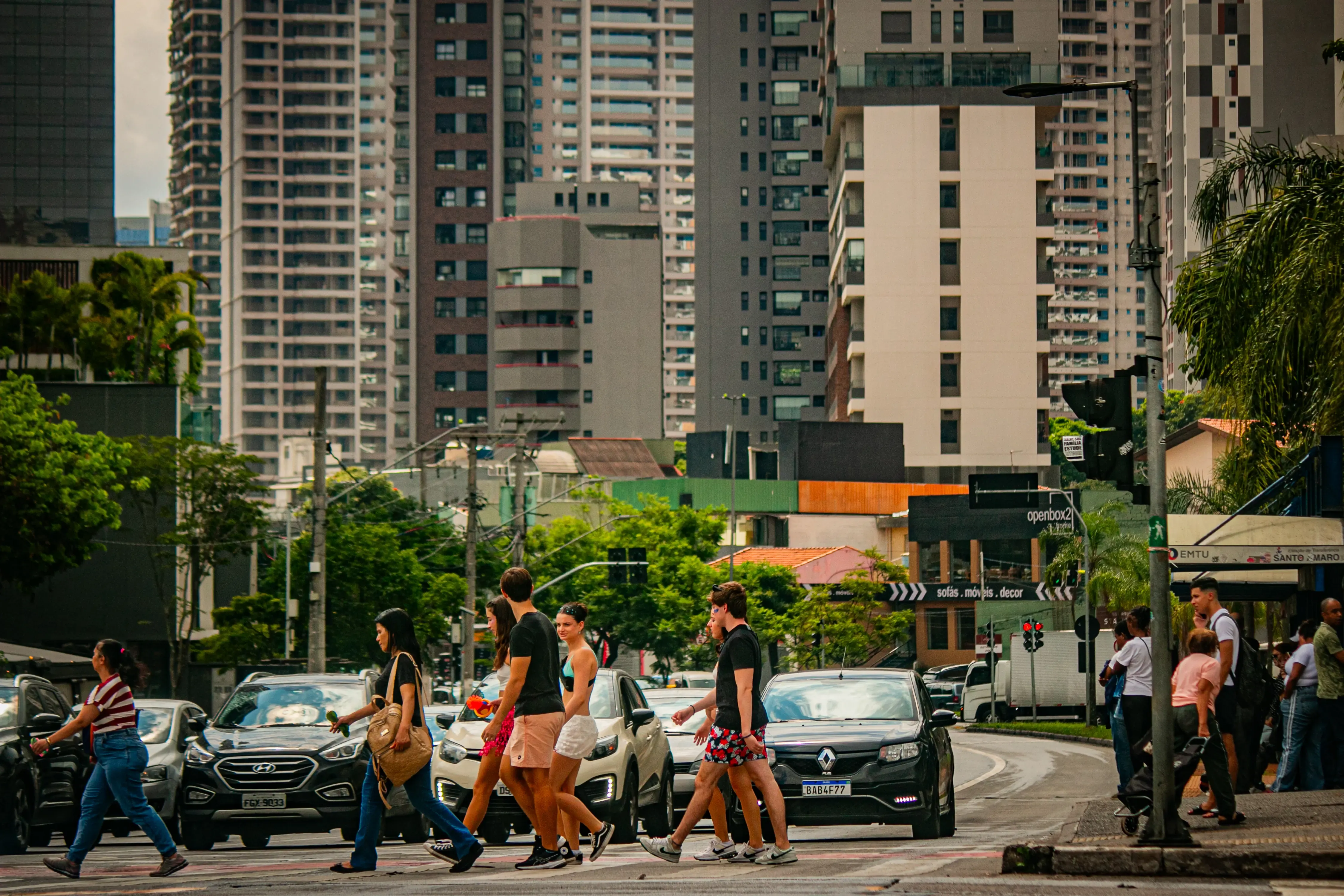 Pedestrians crossing a busy Brooklin avenue with cars and tall apartment buildings in the background