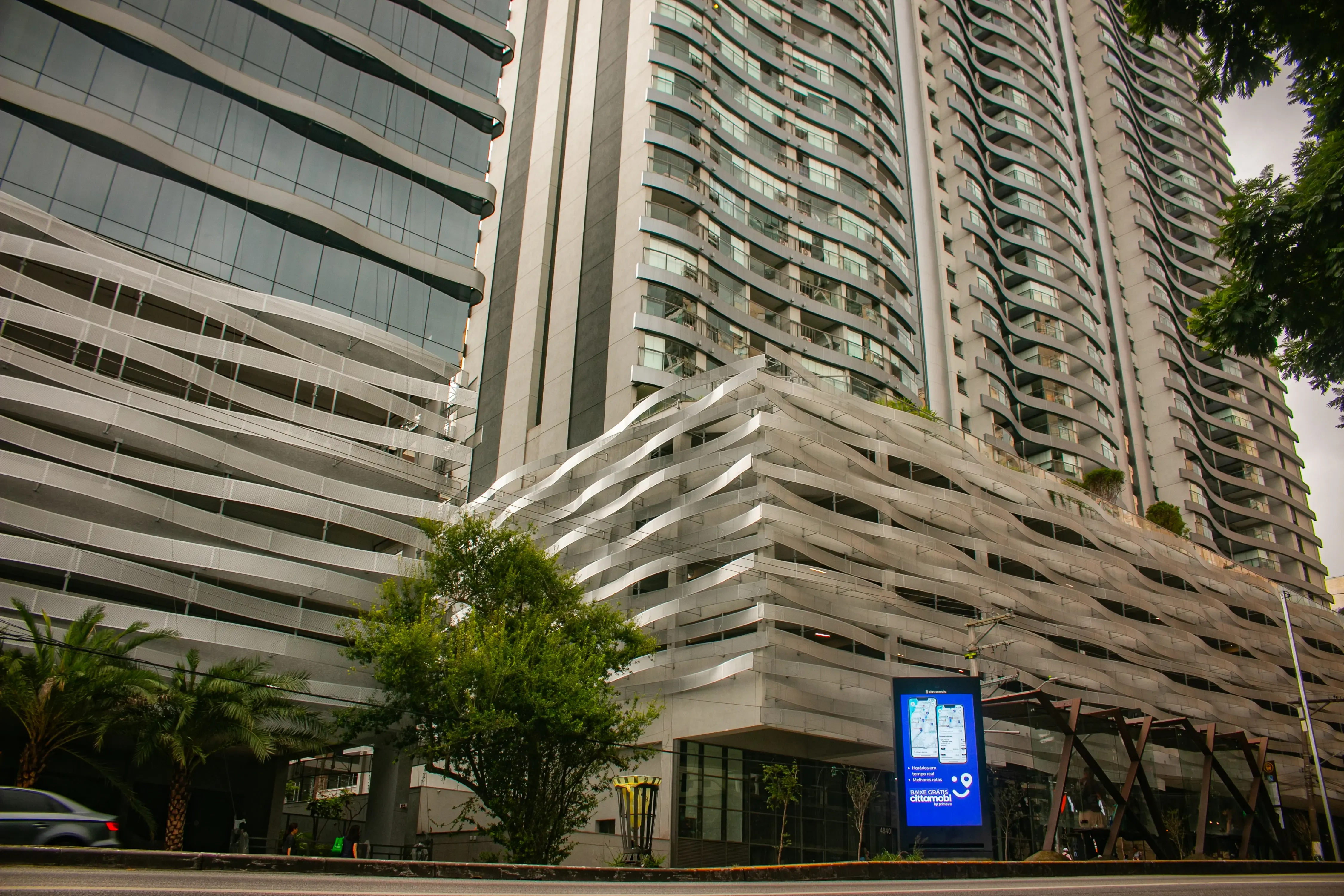 Street-level view of a modern high-rise complex with curved metal architecture and glass towers