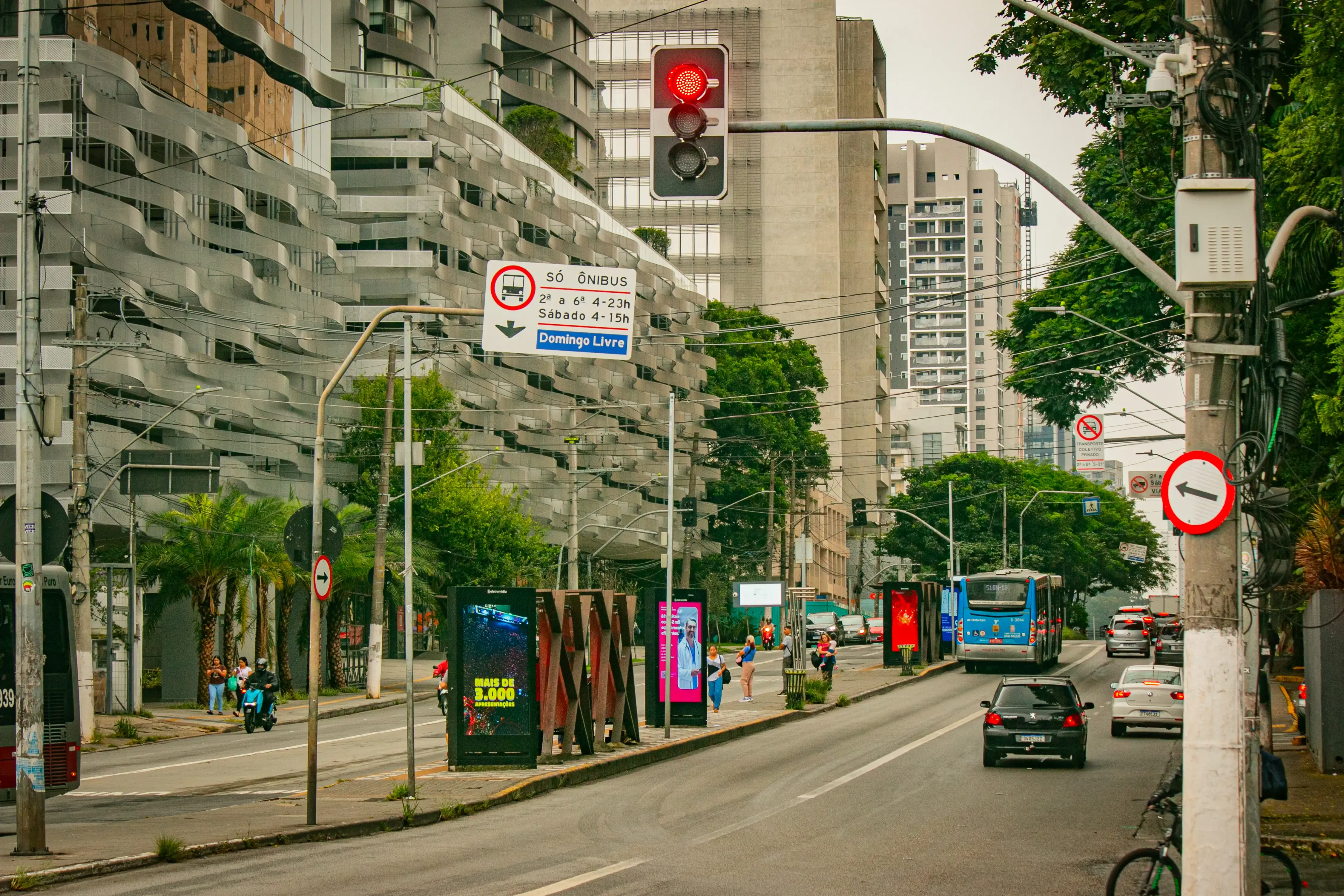 Brooklin avenue with a red traffic light, buses, cars, and modern buildings along both sides of the street
