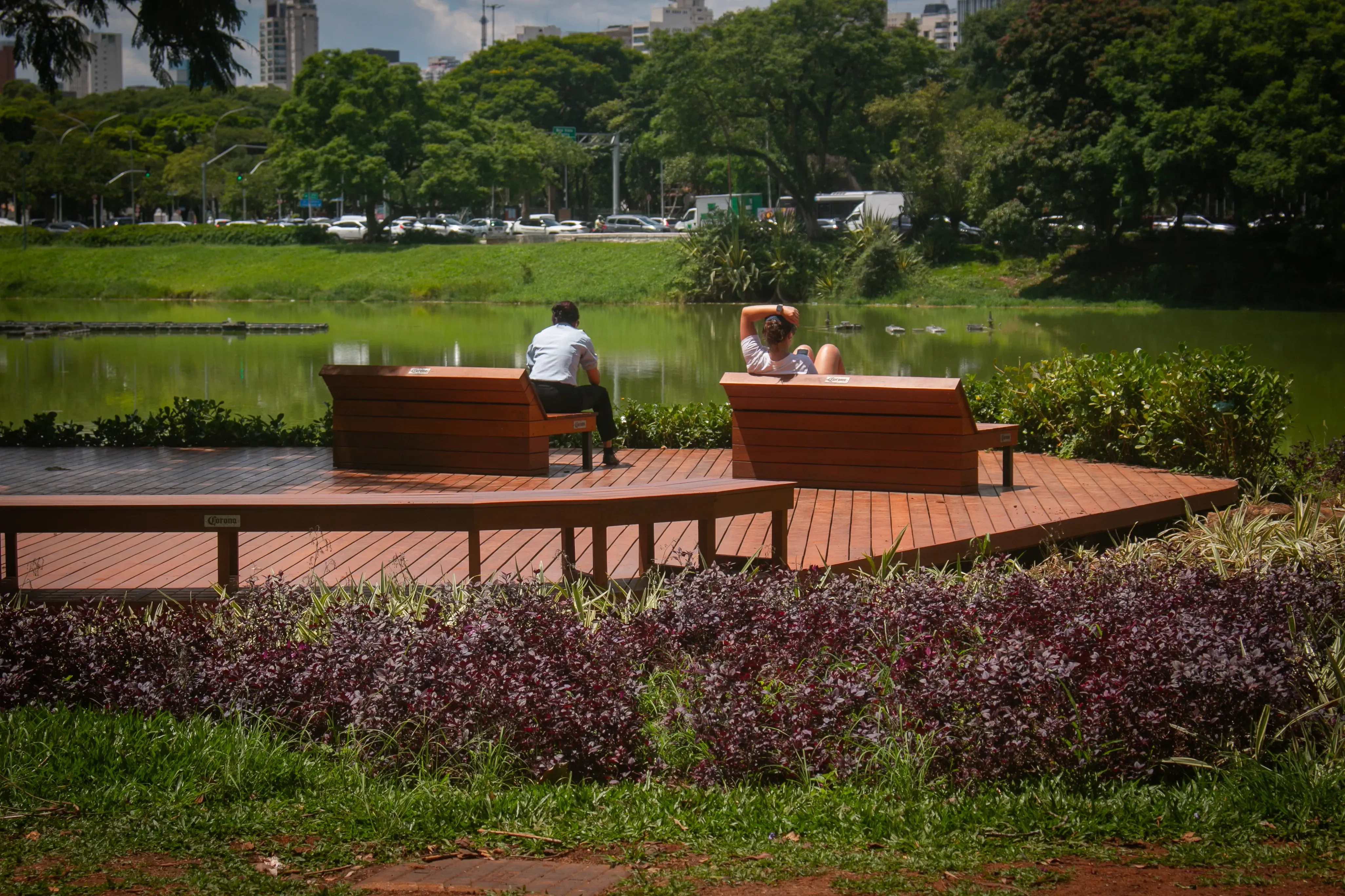 Deck with benches by a lake in Ibirapuera Park, with people relaxing