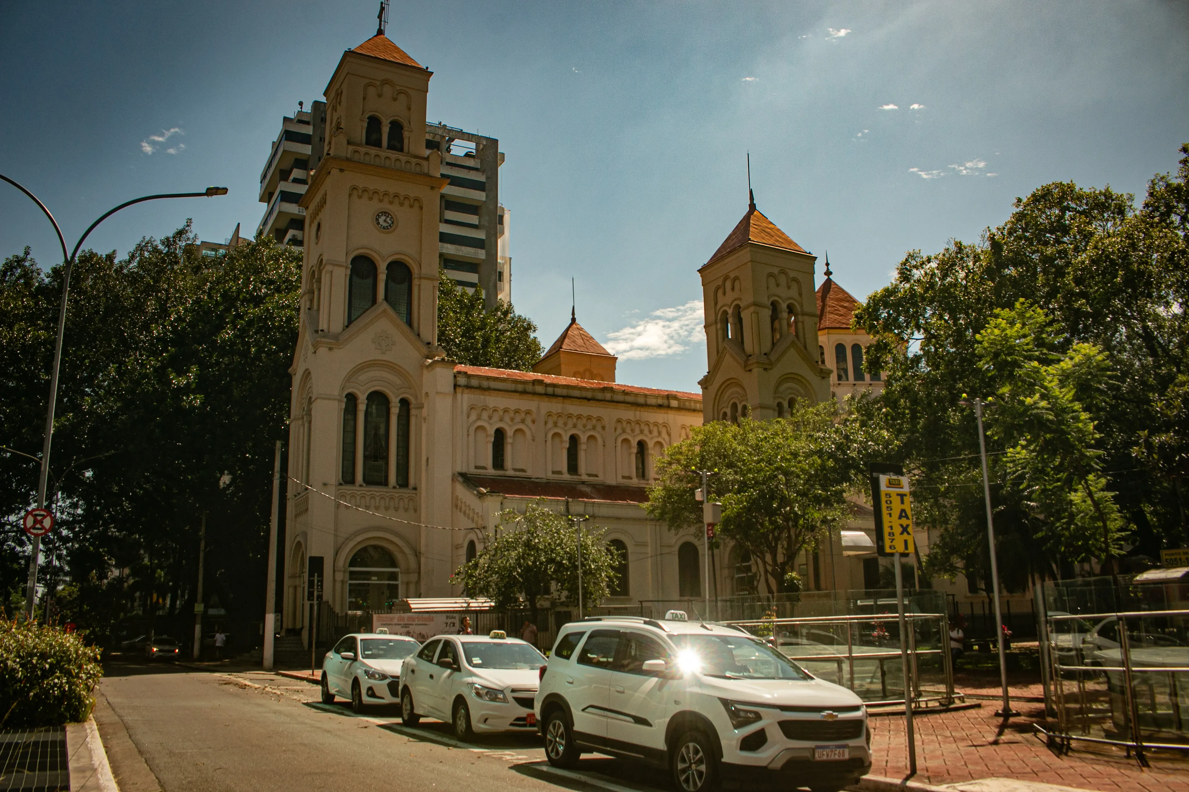 Historic church with twin towers on a sunny street with taxis and trees