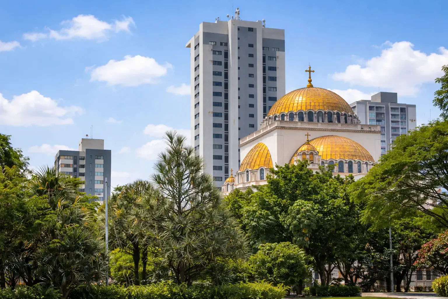 Golden-domed church and modern high-rises viewed from a leafy urban park