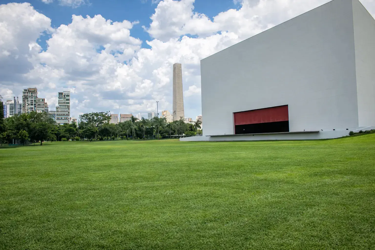 Wide green lawn with a minimalist white pavilion and obelisk at Ibirapuera park