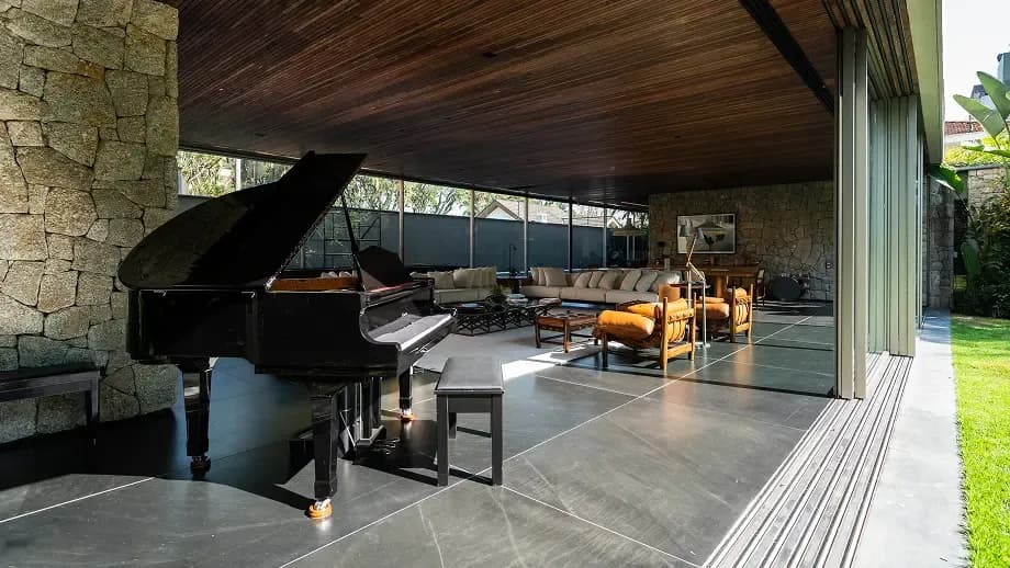 Open-plan modern living space with a grand piano, stone walls, and indoor‑outdoor seating