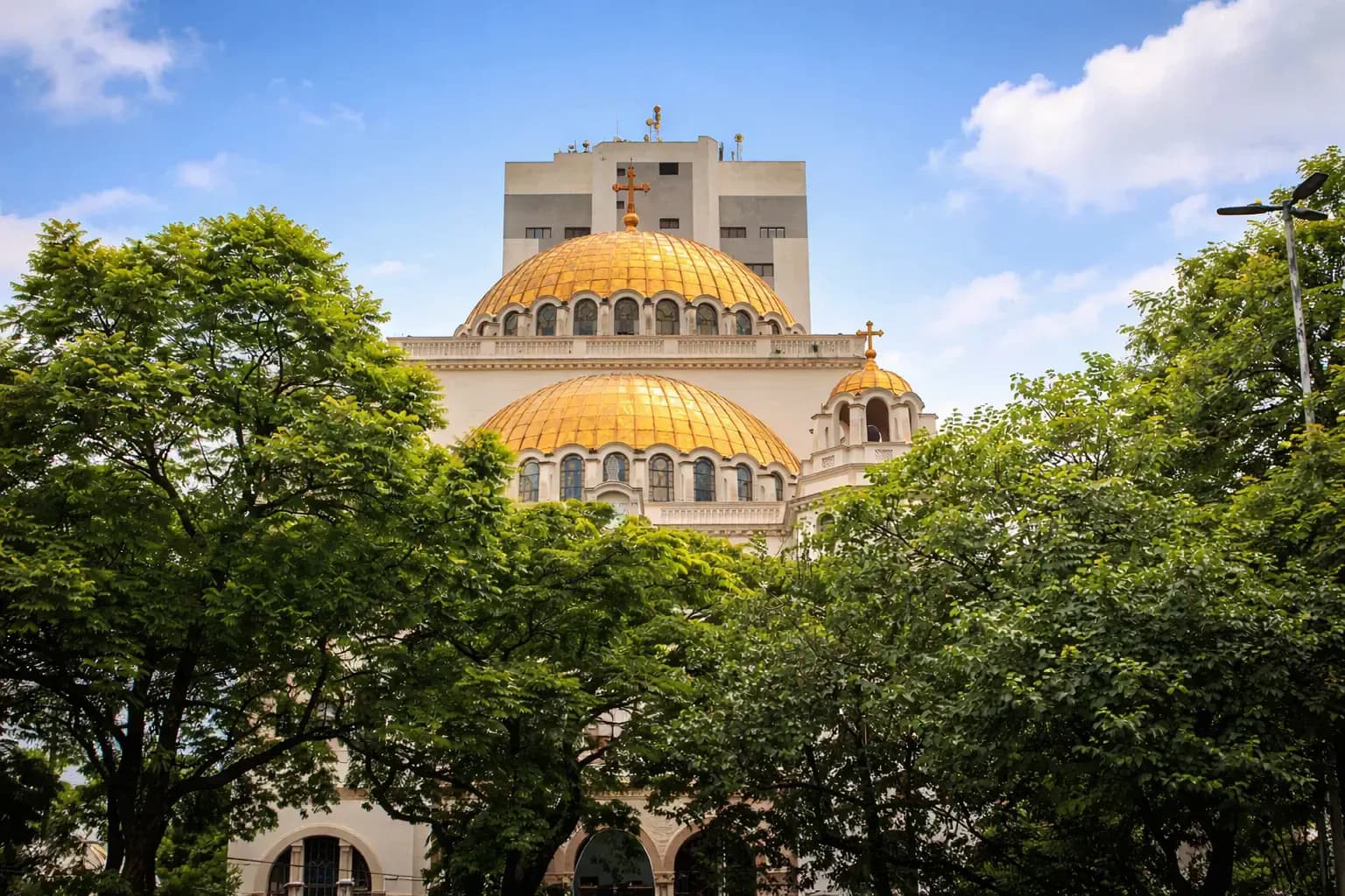 Golden-domed church rising above lush green trees under a bright blue sky