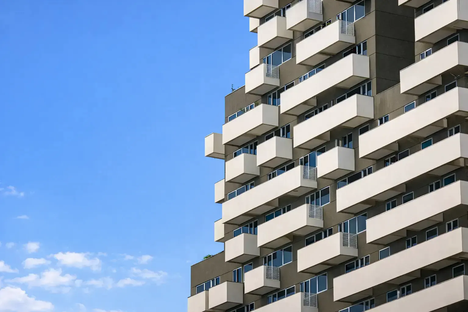 Close-up of a contemporary apartment facade with stacked white balconies against blue sky