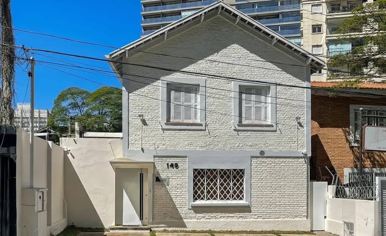 White brick house facade on a sunny street with taller buildings behind