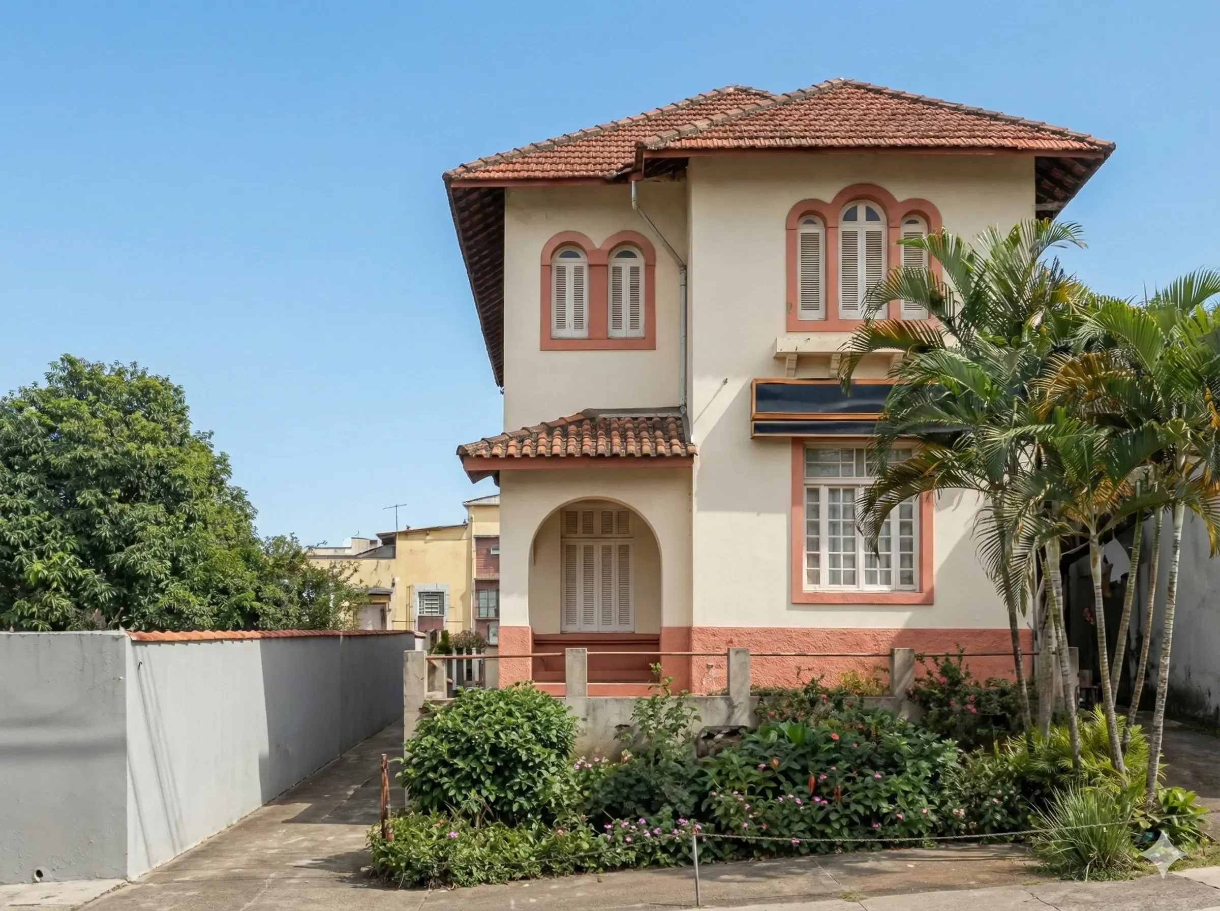Two-story cream house with red roof tiles and palm trees in front