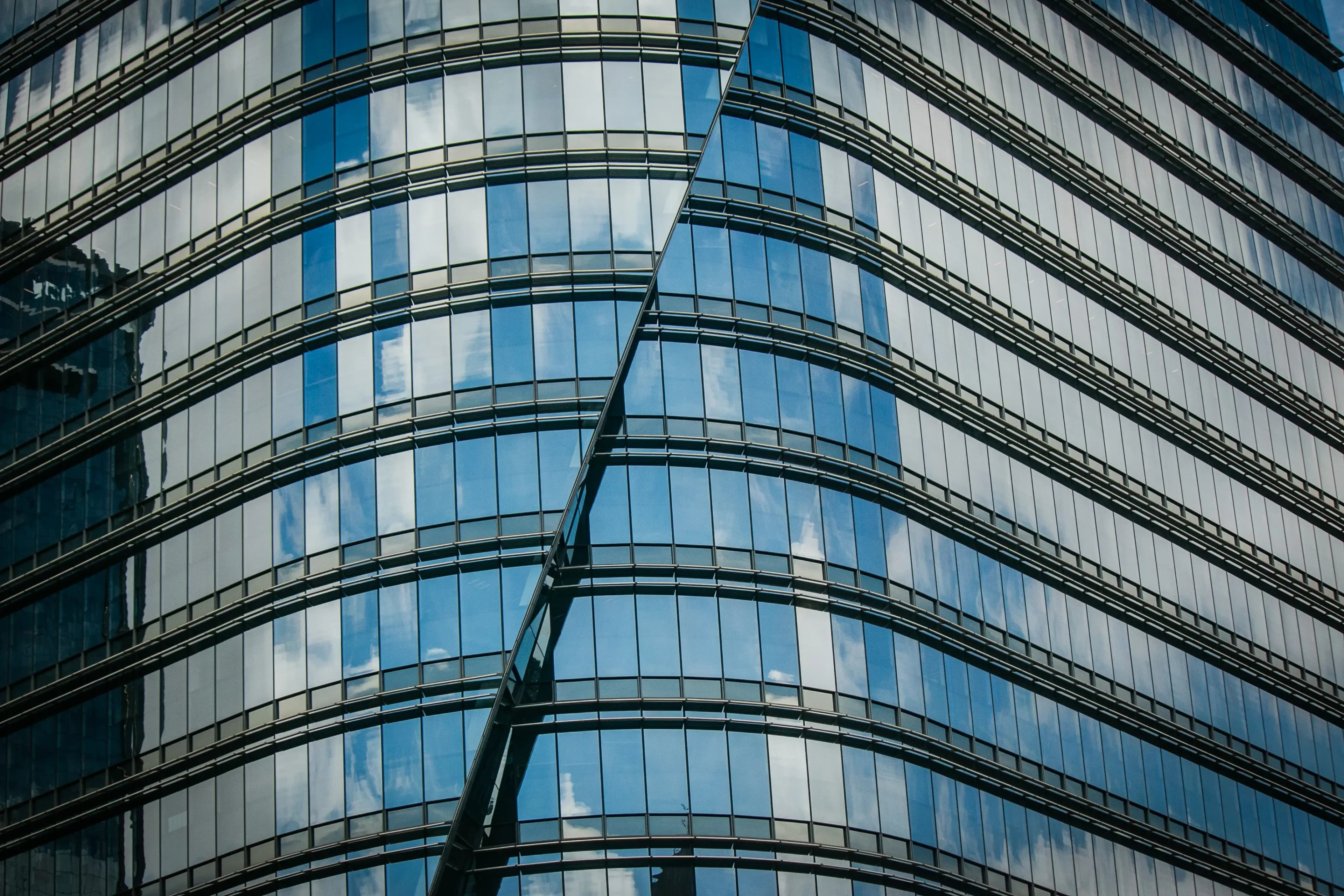 Abstract close-up of a curved glass building facade reflecting the sky